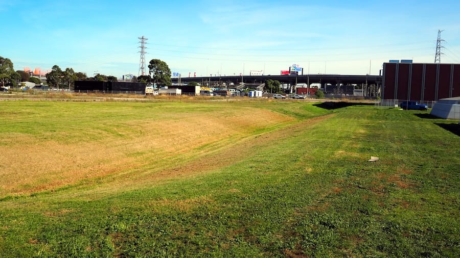 An expanse of grass with a swale, an elevated freeway in the distance and structure on the right.