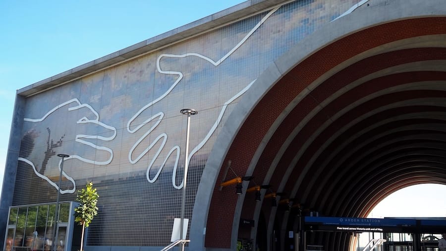 The side of a structure showing the outline of two hands over a mosaic landscape.